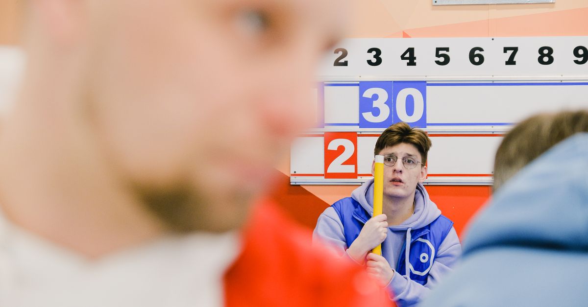Blurred sportsman near male player with worrier face and broom in hands sitting near score board during sportive curling game